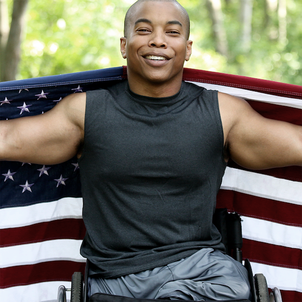 Persons with Disabilities Link Button Image -  a man in a wheelchair in front of a flag